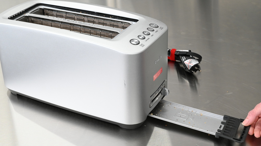 A person emptying the crumb tray on a toaster.