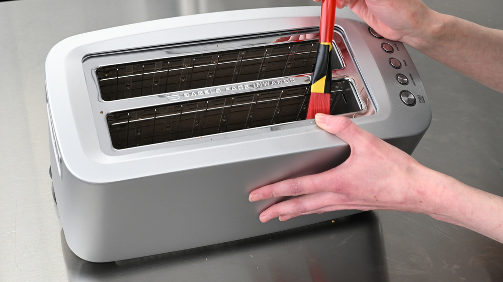A person cleaning inside of a toaster using a brush.