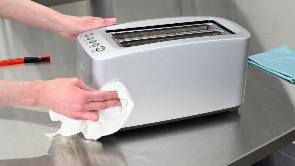 A person cleaning the outside of a toaster using a cloth.