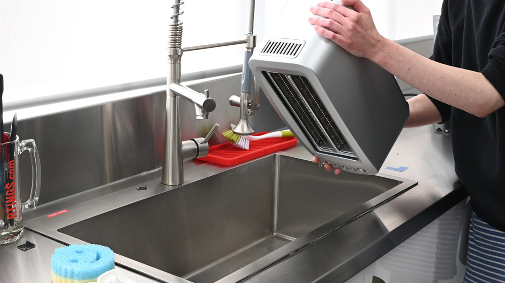 A person shaking out a toaster into a sink.