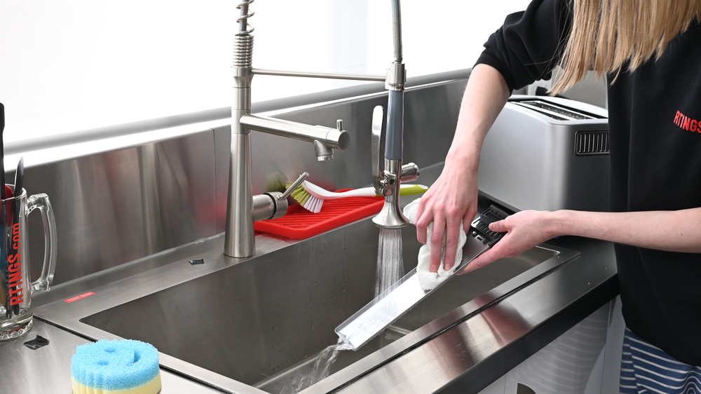 A person washing a crumb tray in a sink.