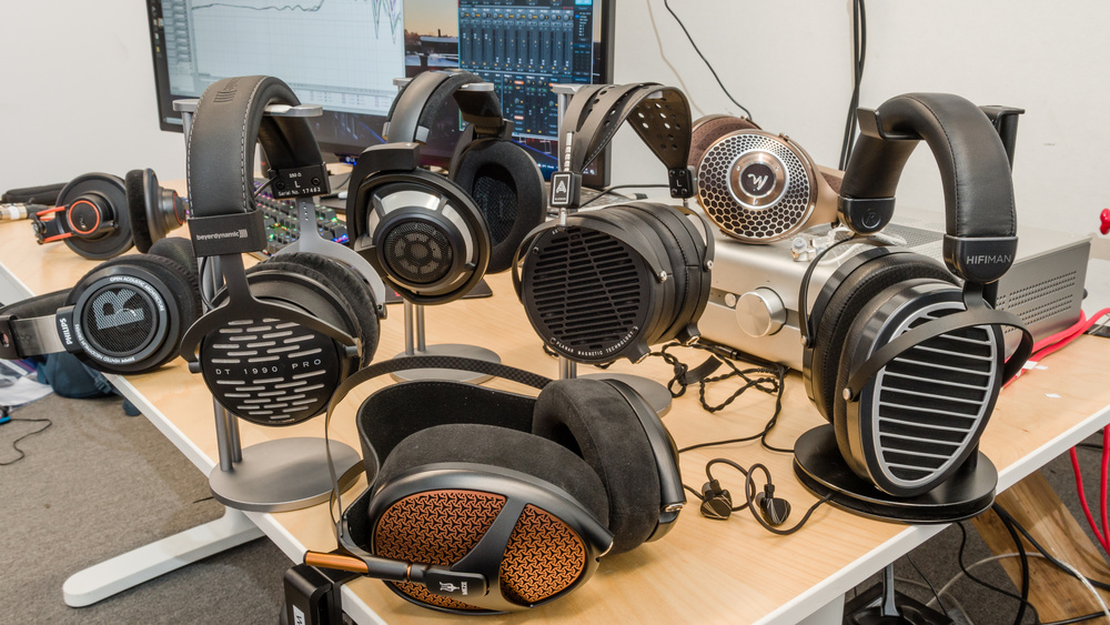A photo shows many audiophile over-ear headphones on a desk in the lab testing setting.